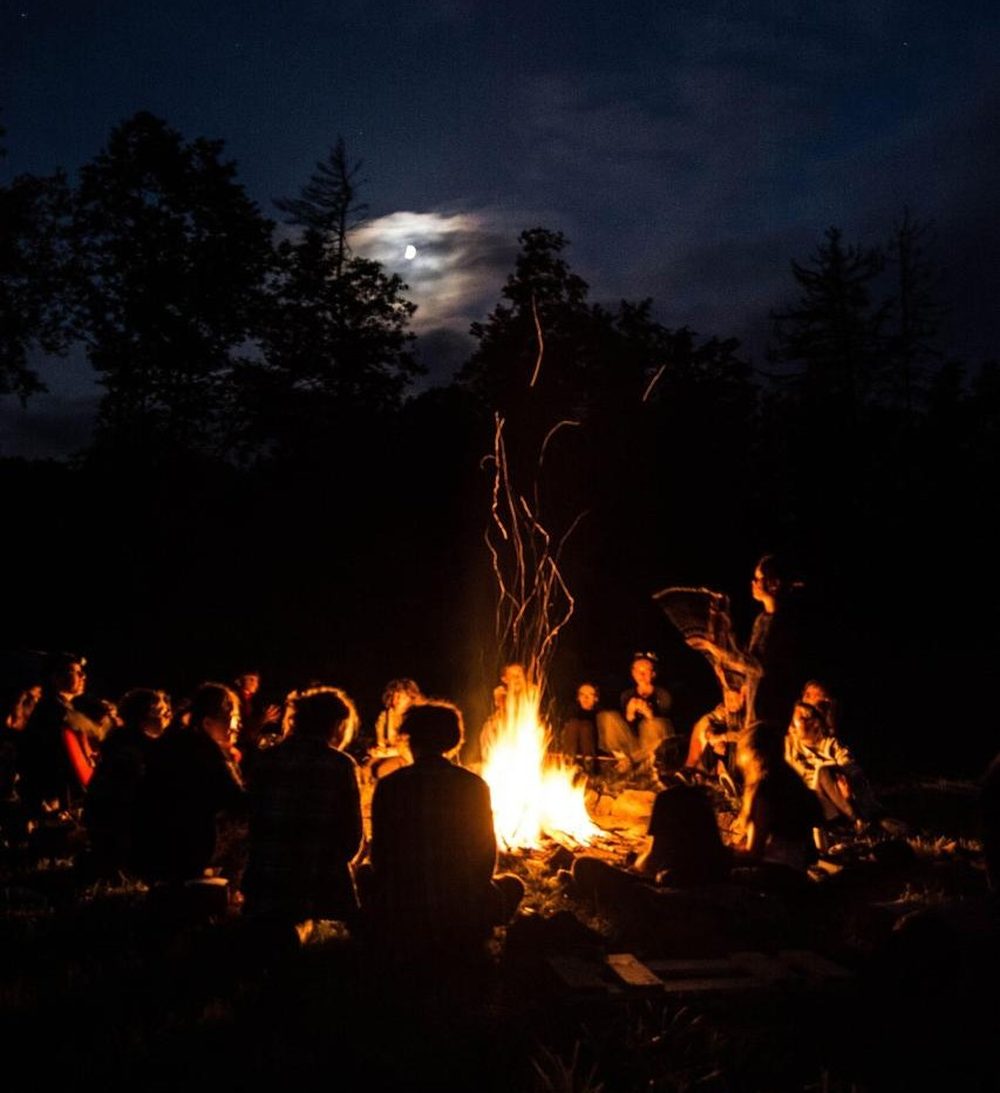 Motorcycle tour guests gathered around a campfire under a moonlit African sky